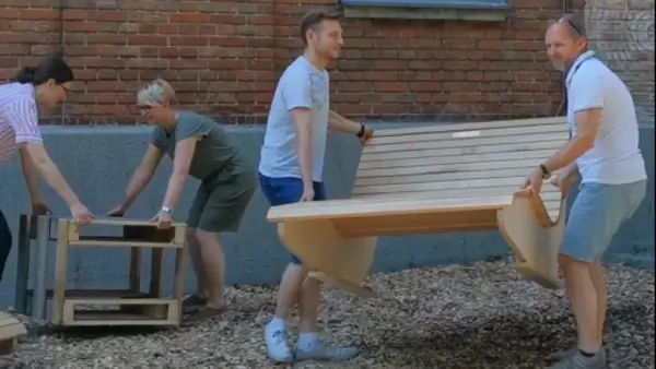 Zwei Männer tragen eine Holzliege, zwei Frauen platzieren einen aus Palettenholz gebauten Tisch